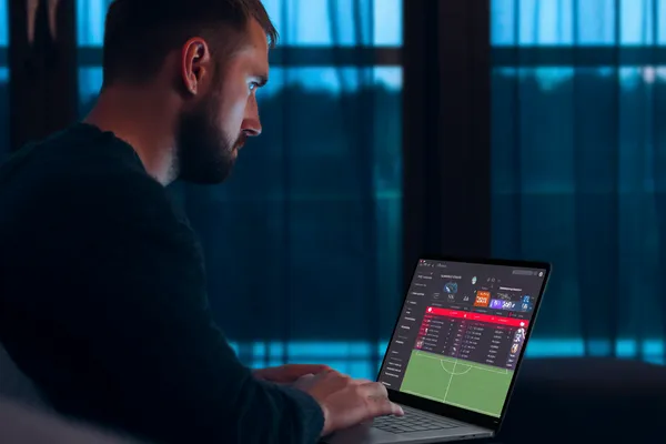 A man focused on his laptop with live stats in the background, highlighting the dedicated sports and gaming features of the CBAJI mobile app.